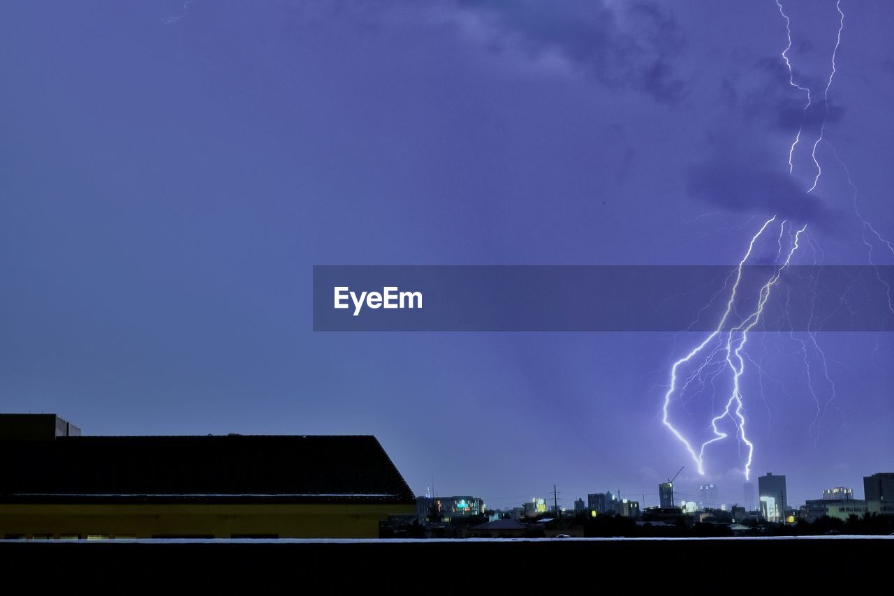 Lightning over illuminated city against blue sky