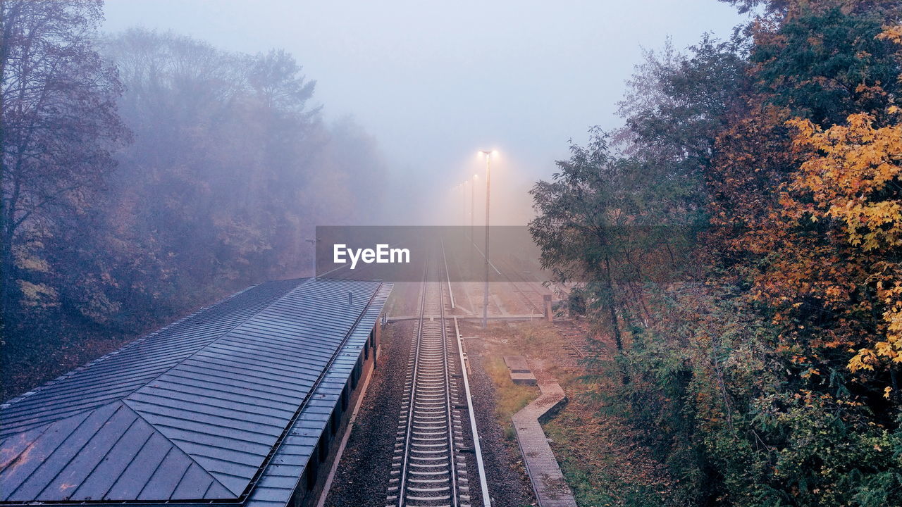 Railroad track amidst trees against foggy sky during autumn