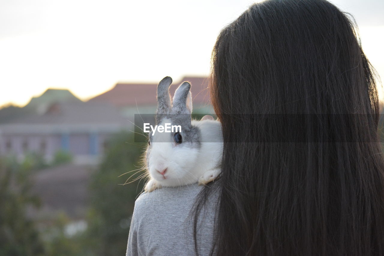 Rear view of woman with rabbit on shoulder against sky