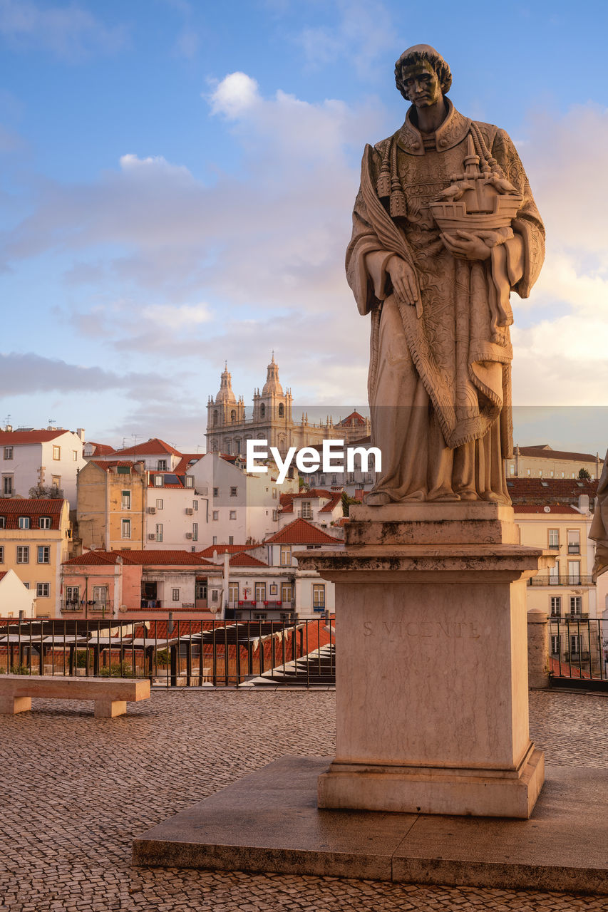 Statue against buildings in city during sunset