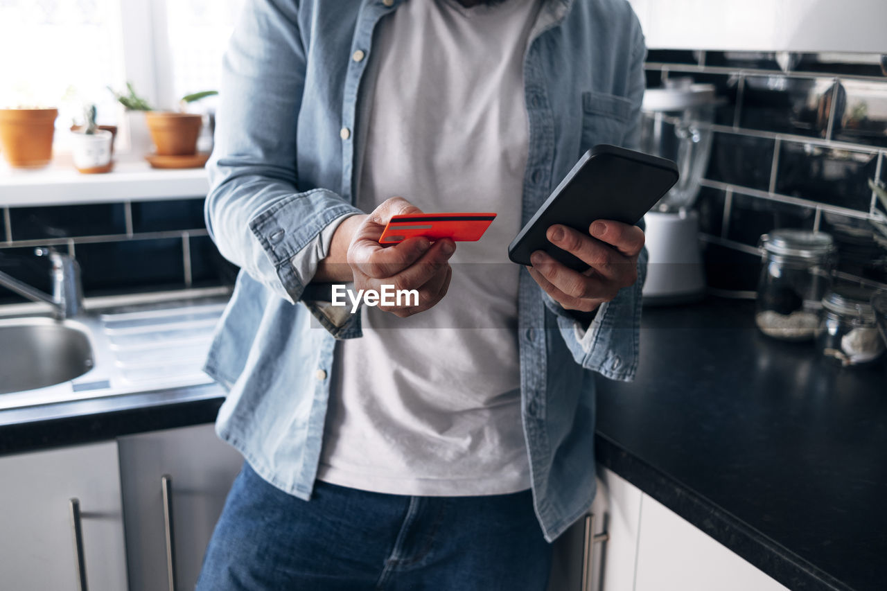 Man with credit card paying bill through smart phone at home