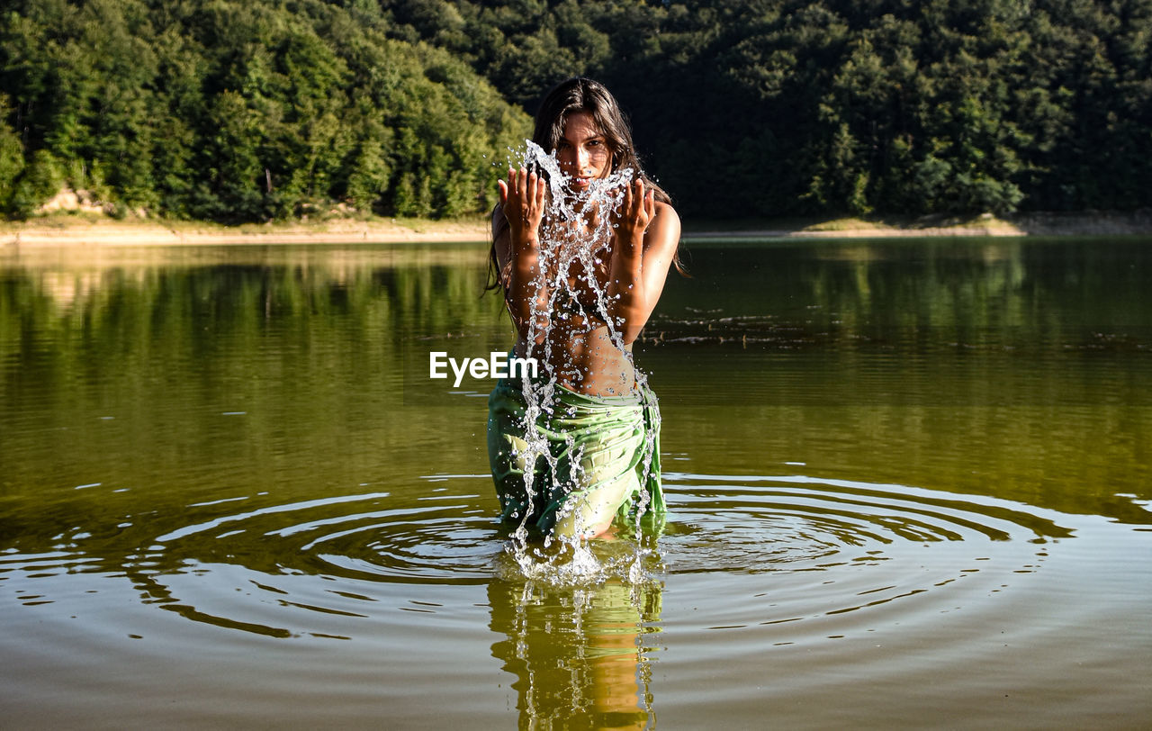 Woman standing by lake against trees