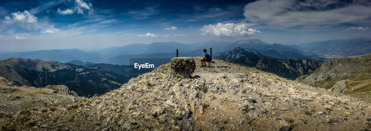 Side view of man sitting on mountain against cloudy sky