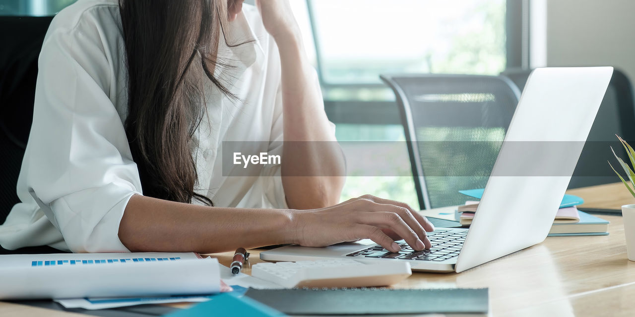 MIDSECTION OF WOMAN USING LAPTOP