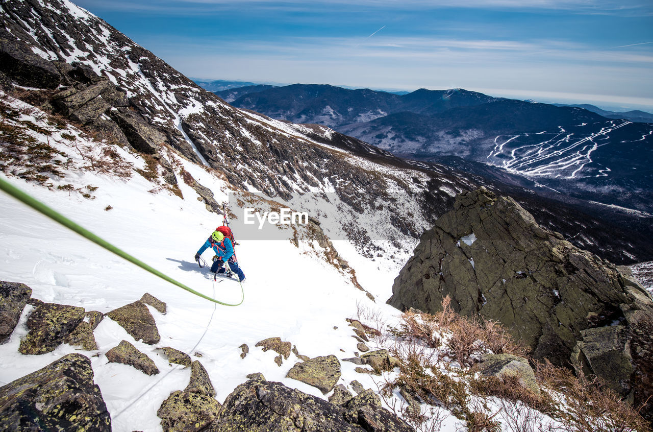 Man climbing steep snow gully with climbing rope and skis