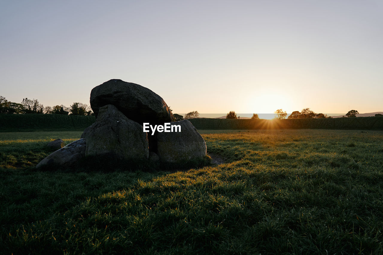 Scenic view of rocks on field against sky during sunset