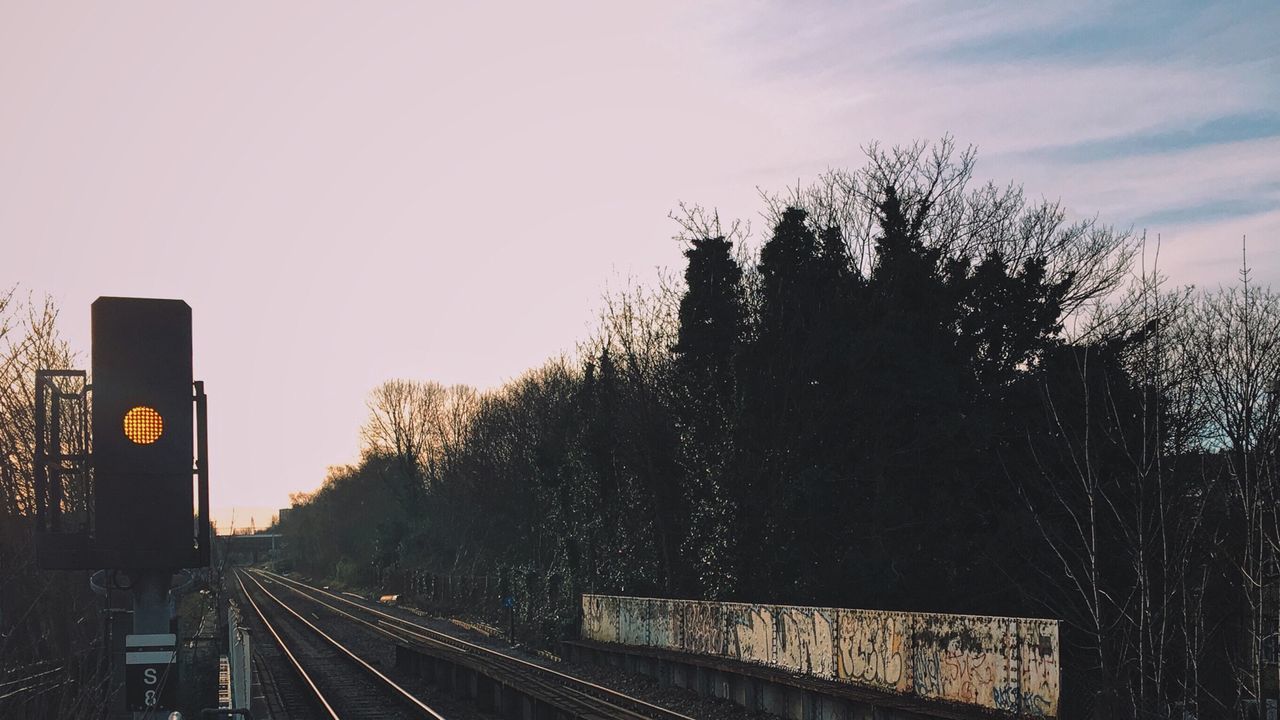 Signal by railroad tracks at sunset