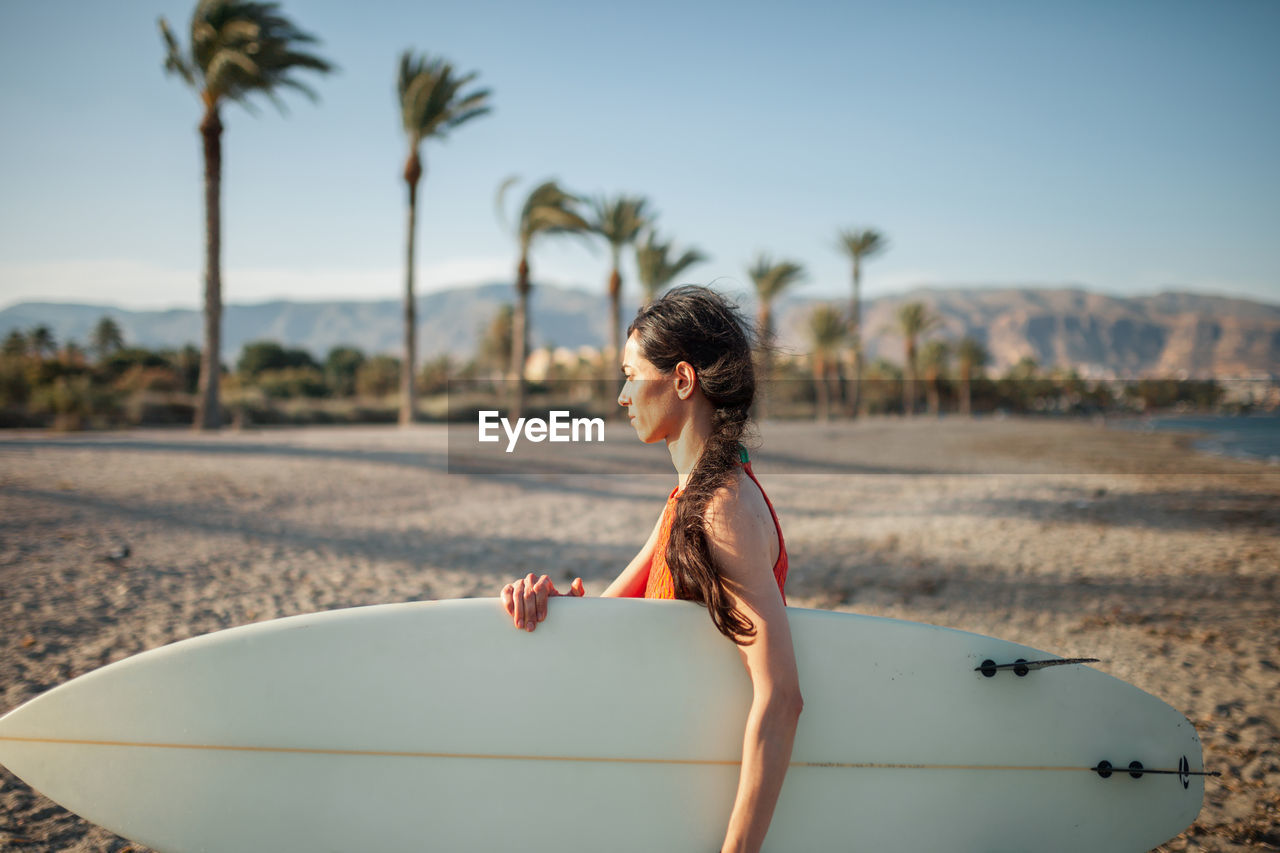 Side view of woman carrying surfboard while walking at beach