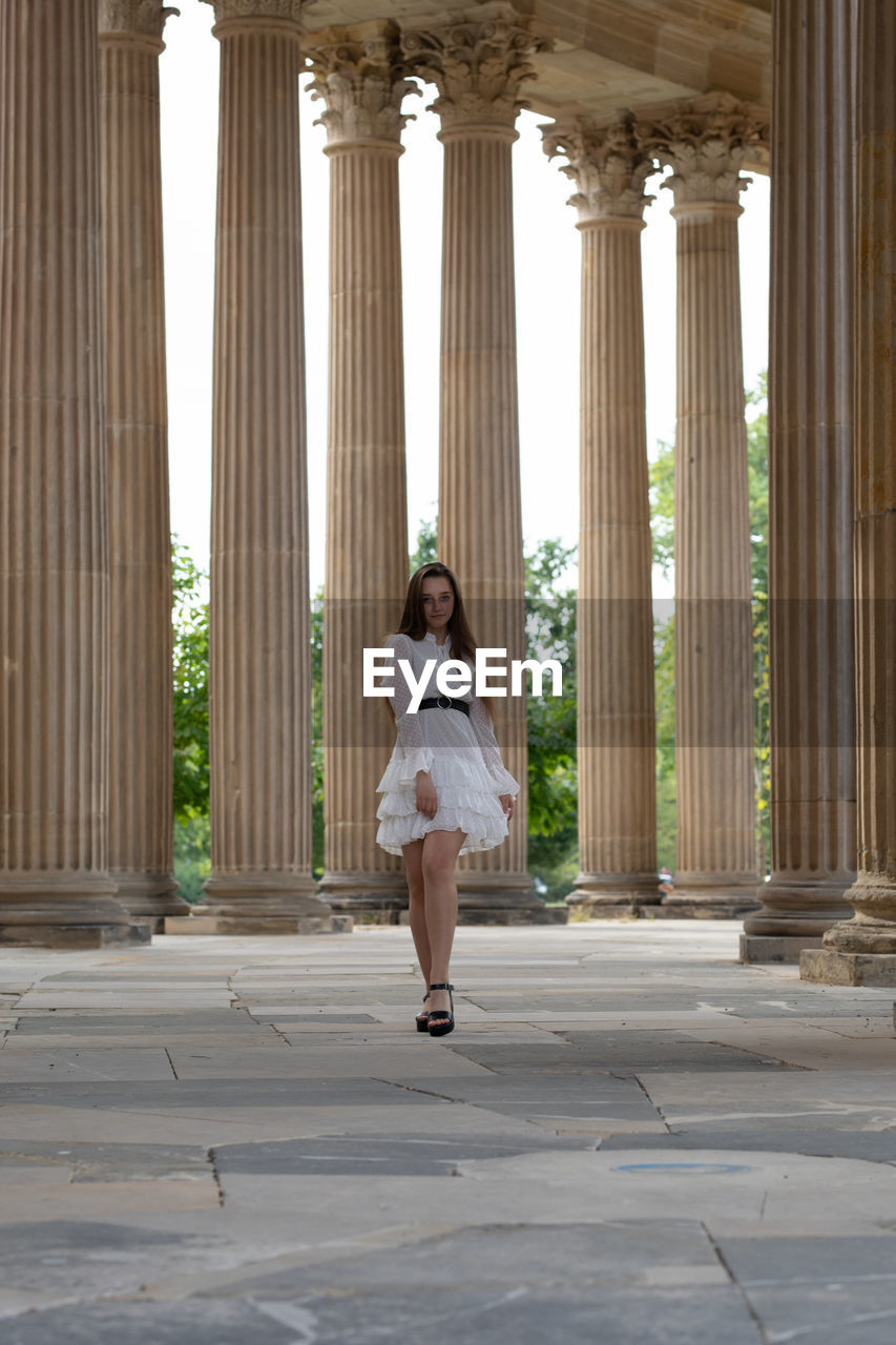 Full length of young woman standing against columns