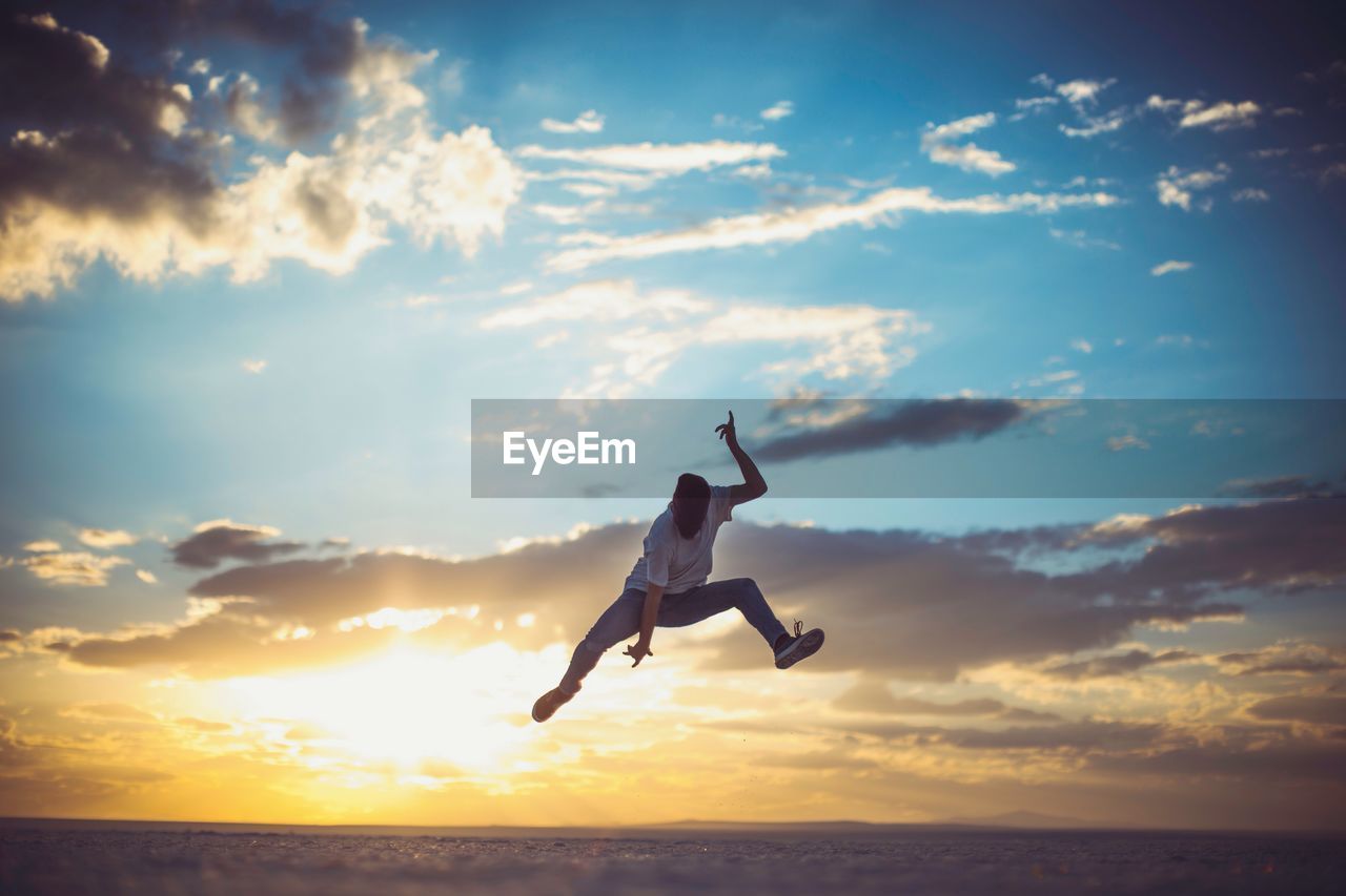 Man jumping over salt flat against sky during sunset