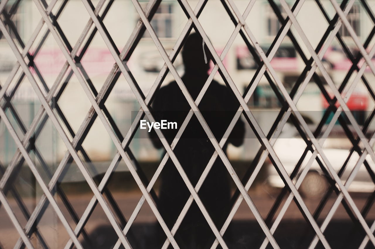 Man reflecting on glass seen through metal grate