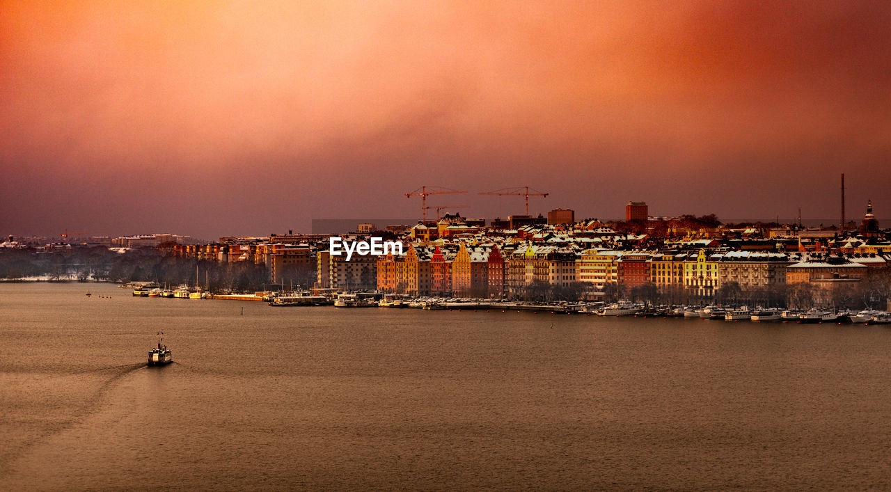 SEA BY BUILDINGS AGAINST SKY AT SUNSET