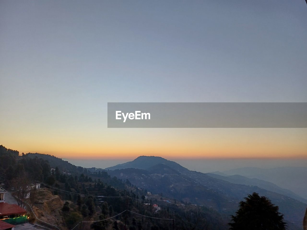 sky, mountain, scenics - nature, beauty in nature, tree, landscape, environment, nature, sunset, dawn, mountain range, architecture, tranquility, tranquil scene, plant, no people, travel destinations, evening, built structure, copy space, travel, building exterior, land, building, outdoors, horizon, clear sky, city, idyllic, cloud, high angle view, tourism, blue, forest, twilight