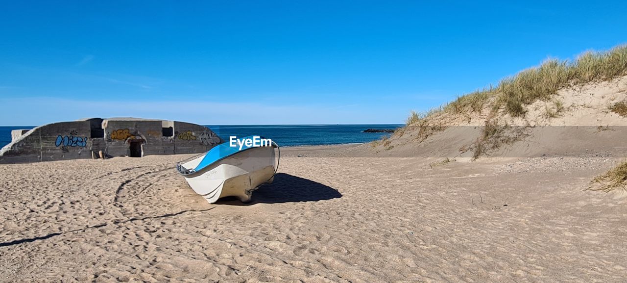 land, sand, beach, sky, sea, nature, natural environment, water, blue, scenics - nature, shore, coast, travel destinations, clear sky, sand dune, travel, sunny, no people, ocean, singing sand, tranquility, beauty in nature, sunlight, landscape, environment, vacation, day, trip, holiday, dune, tourism, summer, outdoors, tranquil scene, horizon, non-urban scene, coastline, body of water