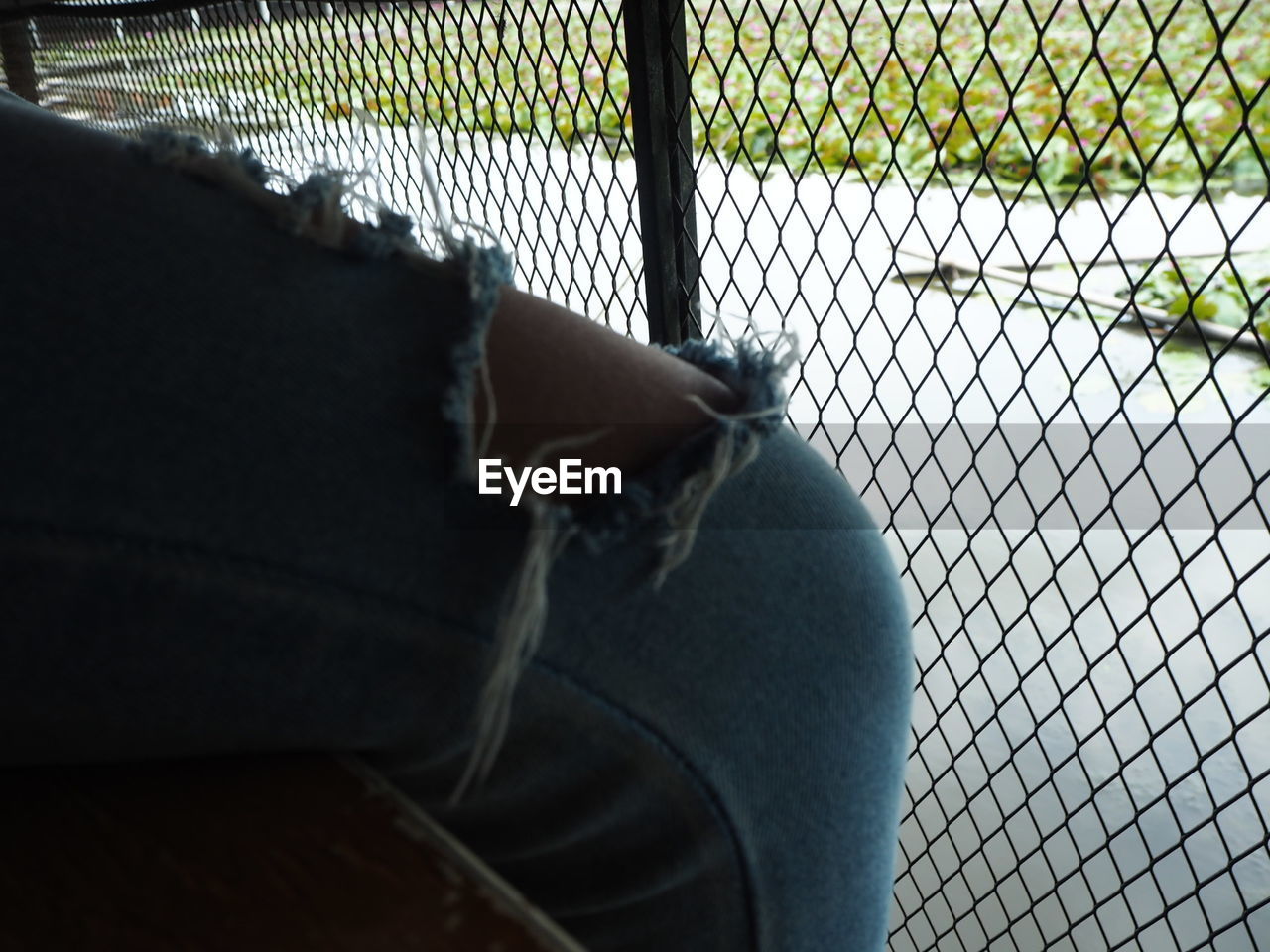 LOW SECTION OF PERSON BY CHAINLINK FENCE AGAINST ROAD