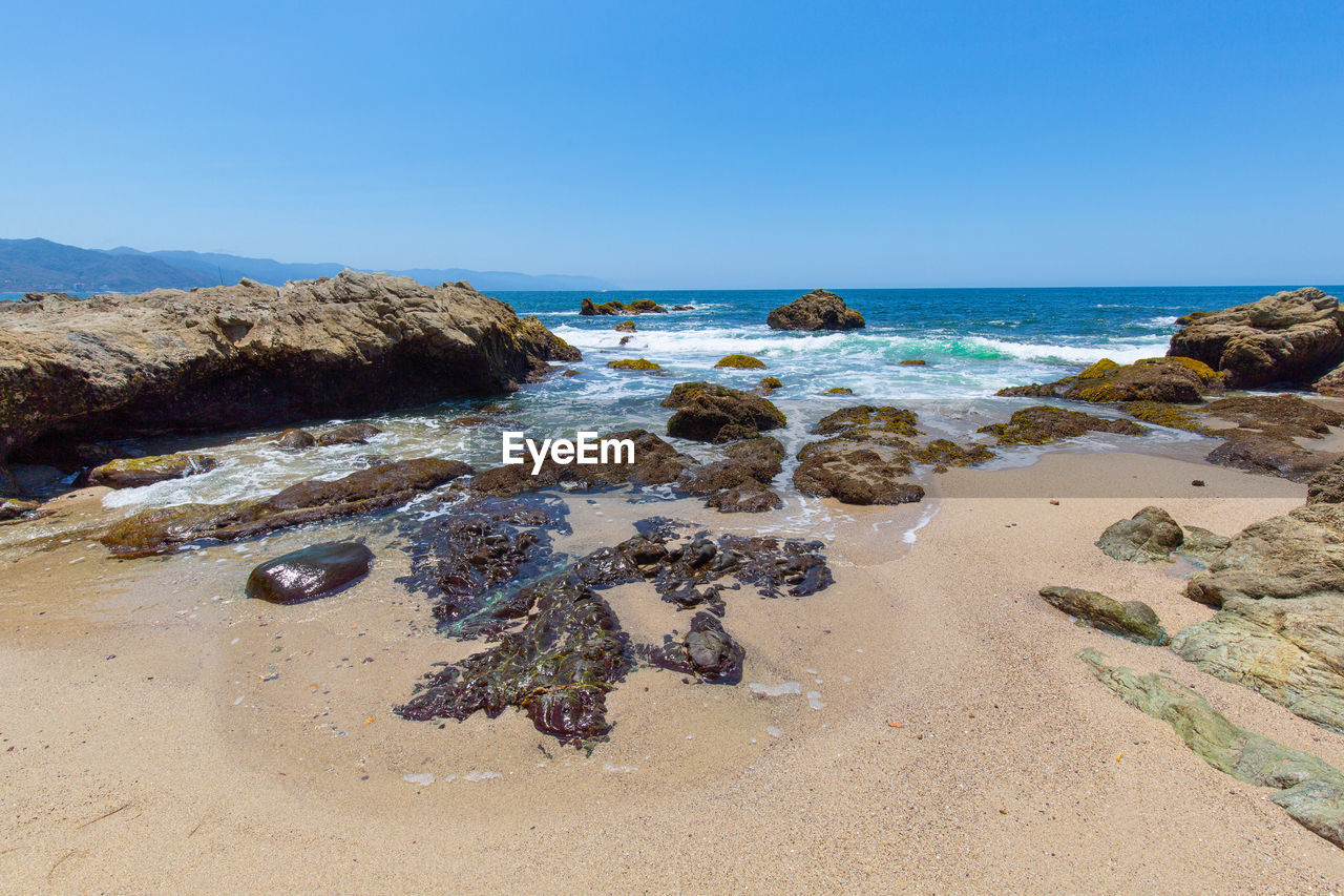 ROCKS ON SHORE AGAINST CLEAR SKY