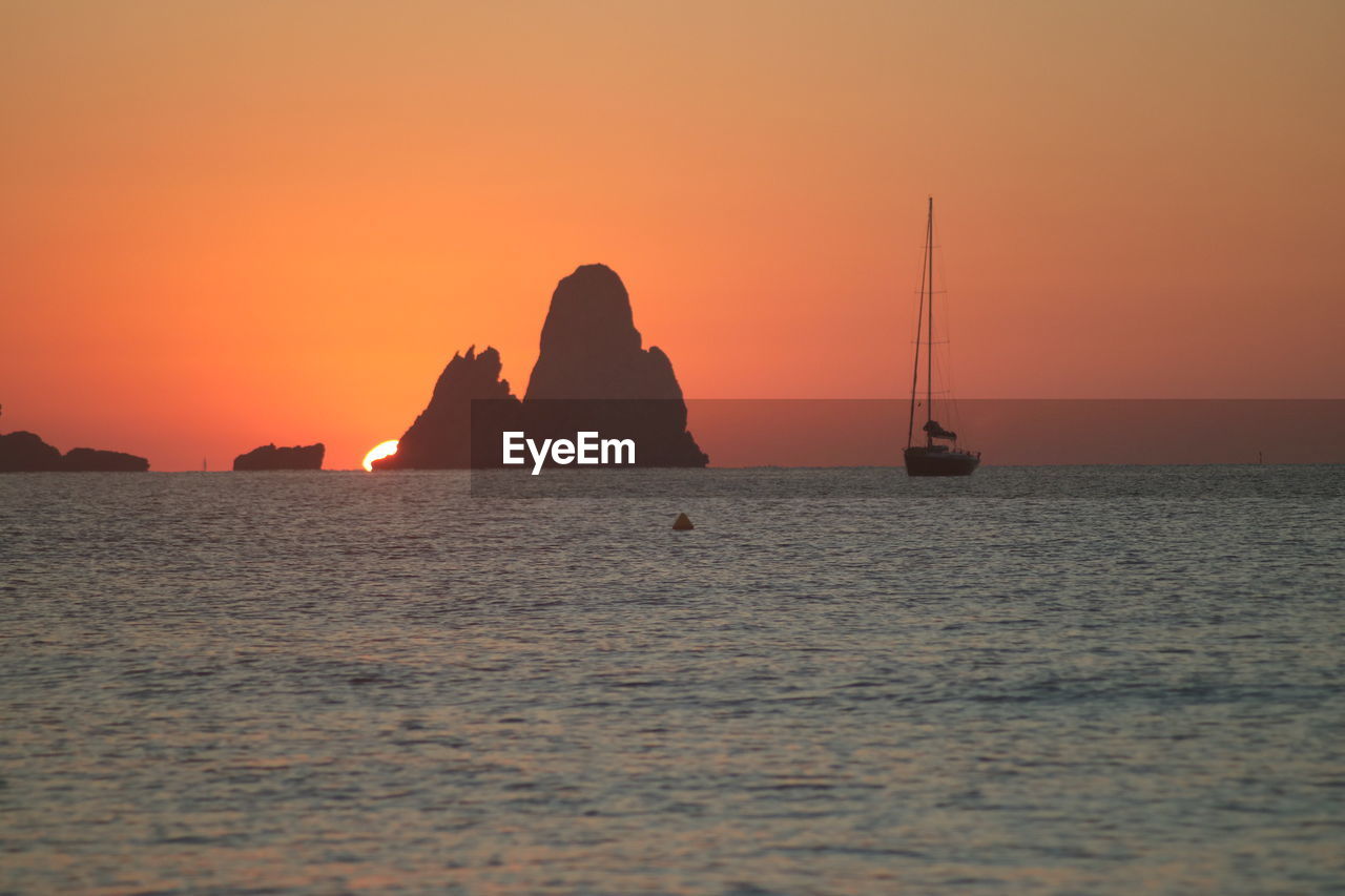 SILHOUETTE ROCKS BY SEA AGAINST ORANGE SKY