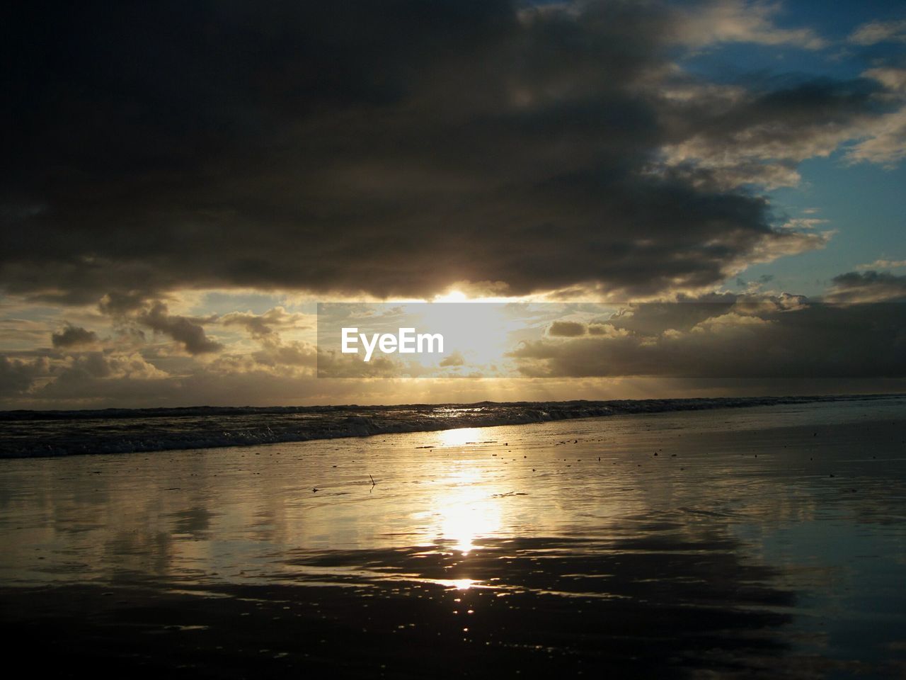 Scenic view of beach against cloudy sky during sunset