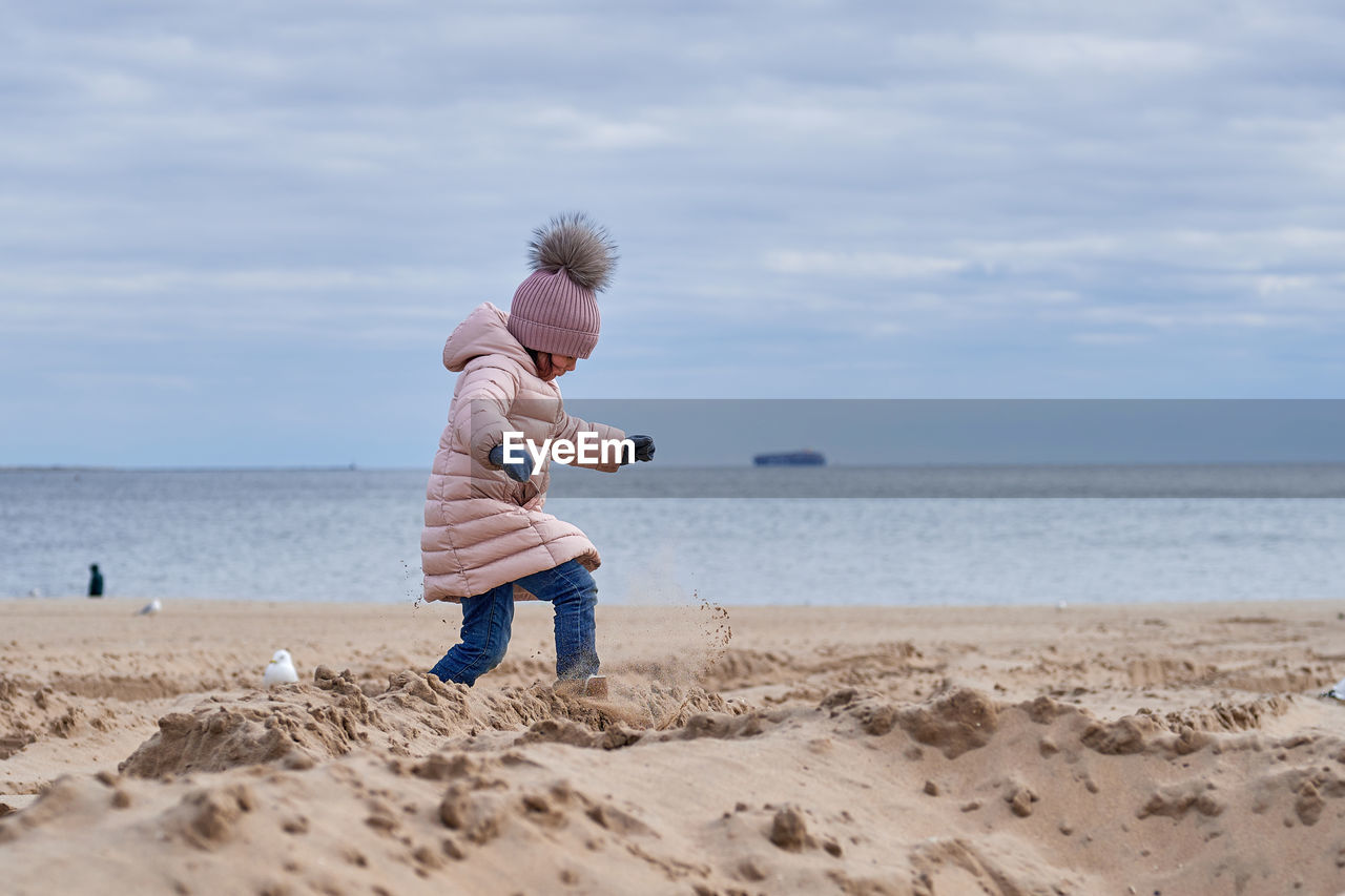 Cute girl fooling around at the beach in a winter coat