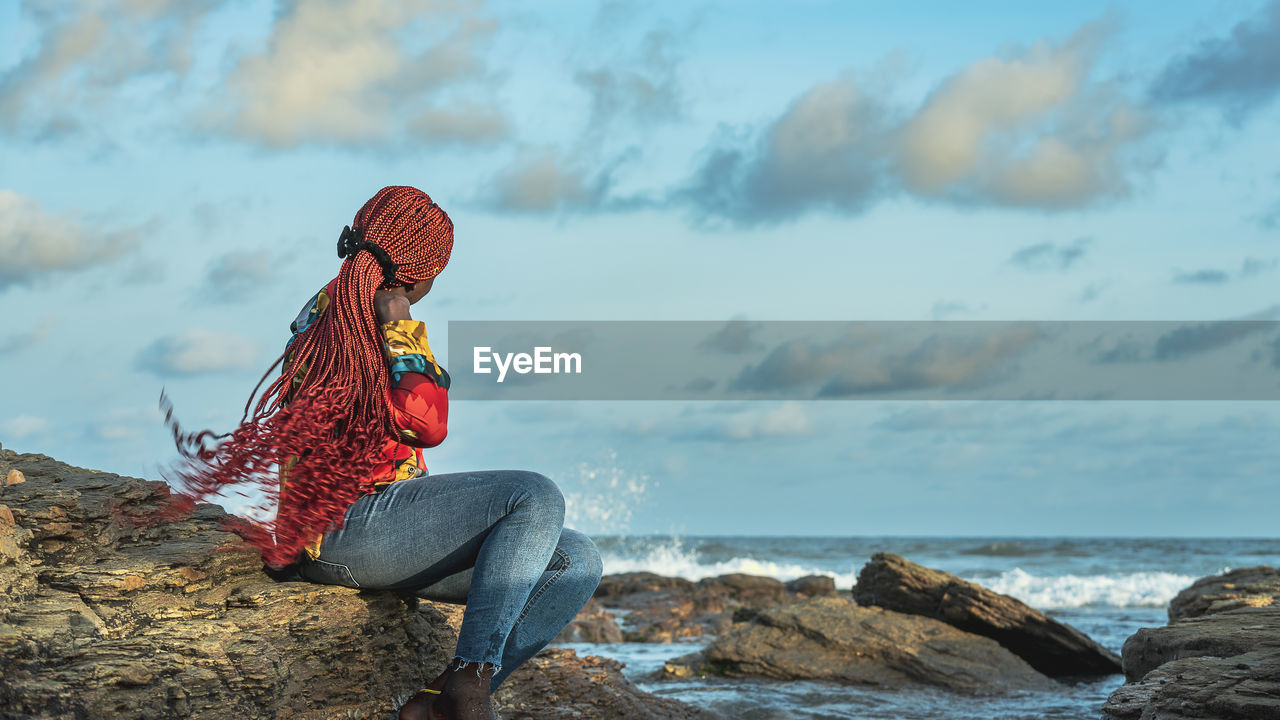 Rear view of woman sitting on rock at beach