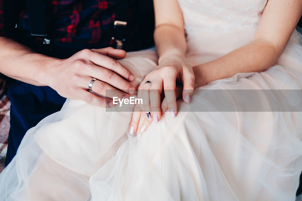 Midsection of bride and groom in wedding dress sitting on bed