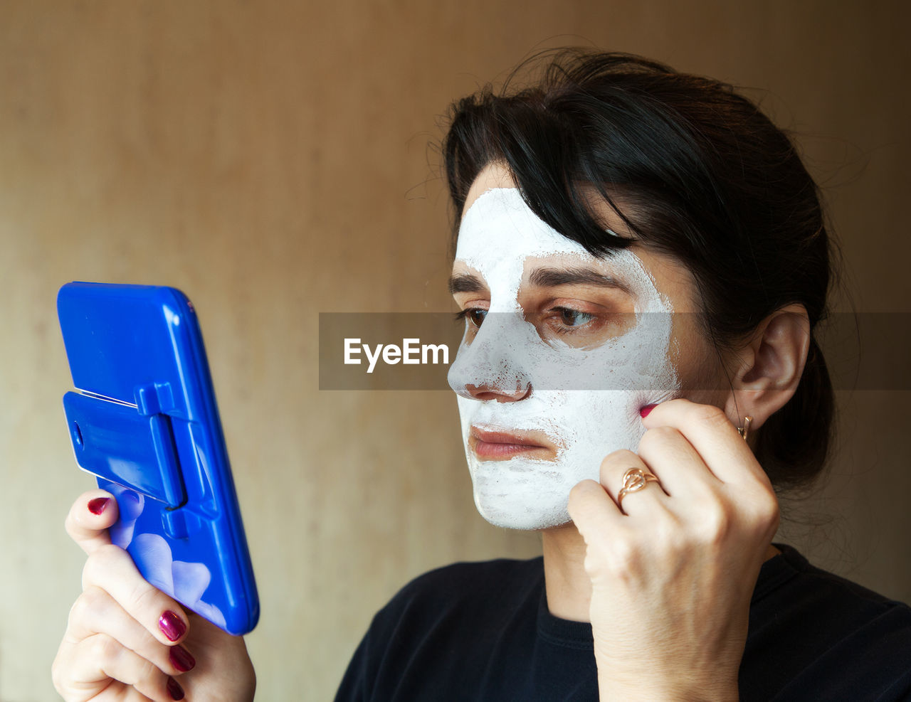 Woman wearing facial mask while looking in hand mirror at home