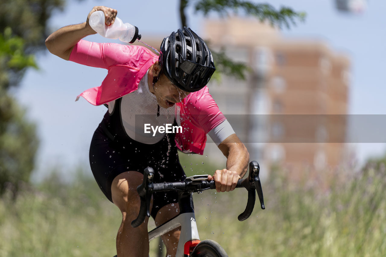 Cyclist riding bicycle pouring water from bottle on sunny day