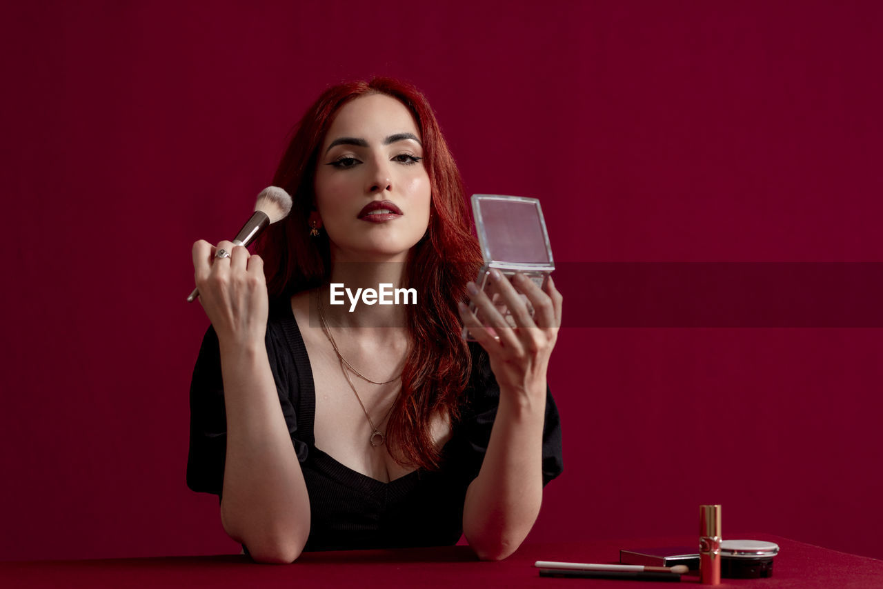 Woman looking at camera while holding makeup brushes against an isolated background.