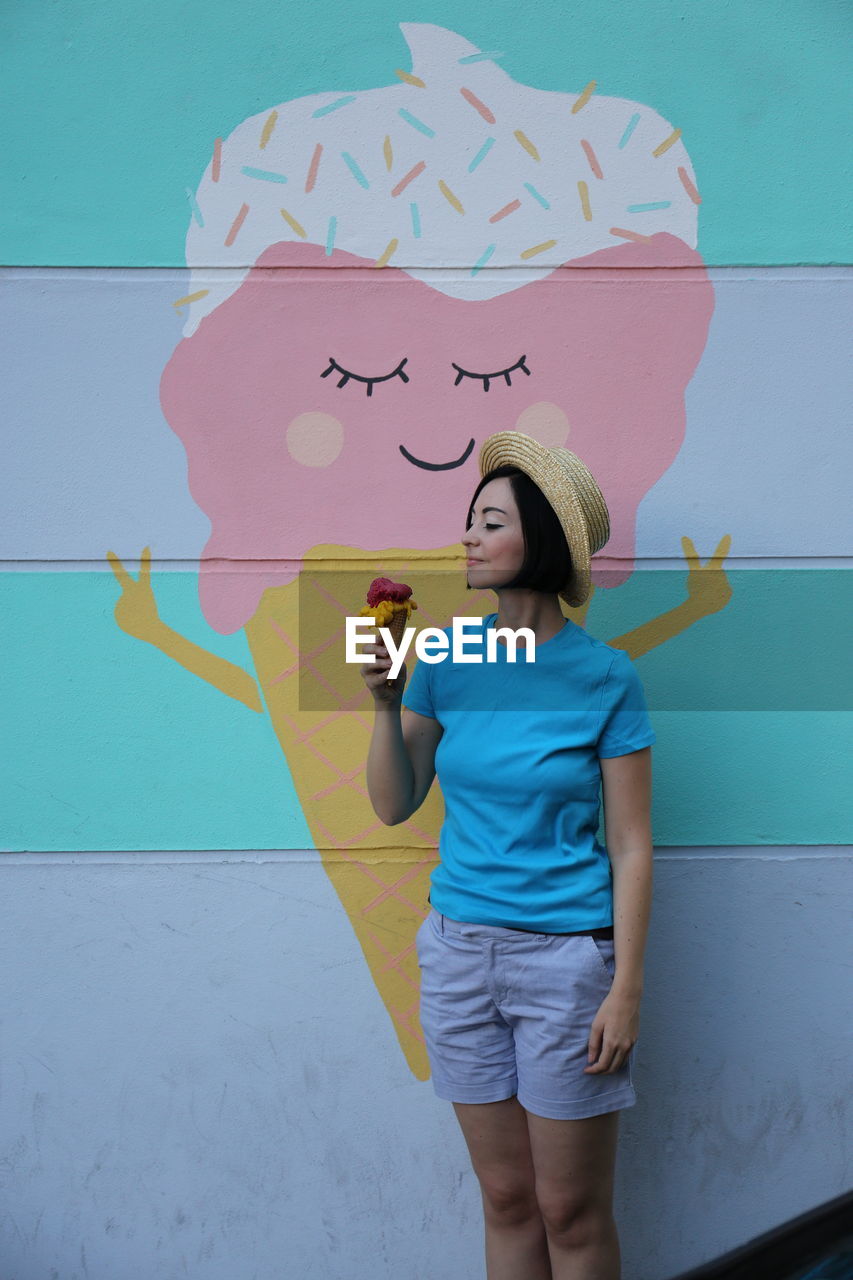 Woman holding ice cream cone while standing against mural wall