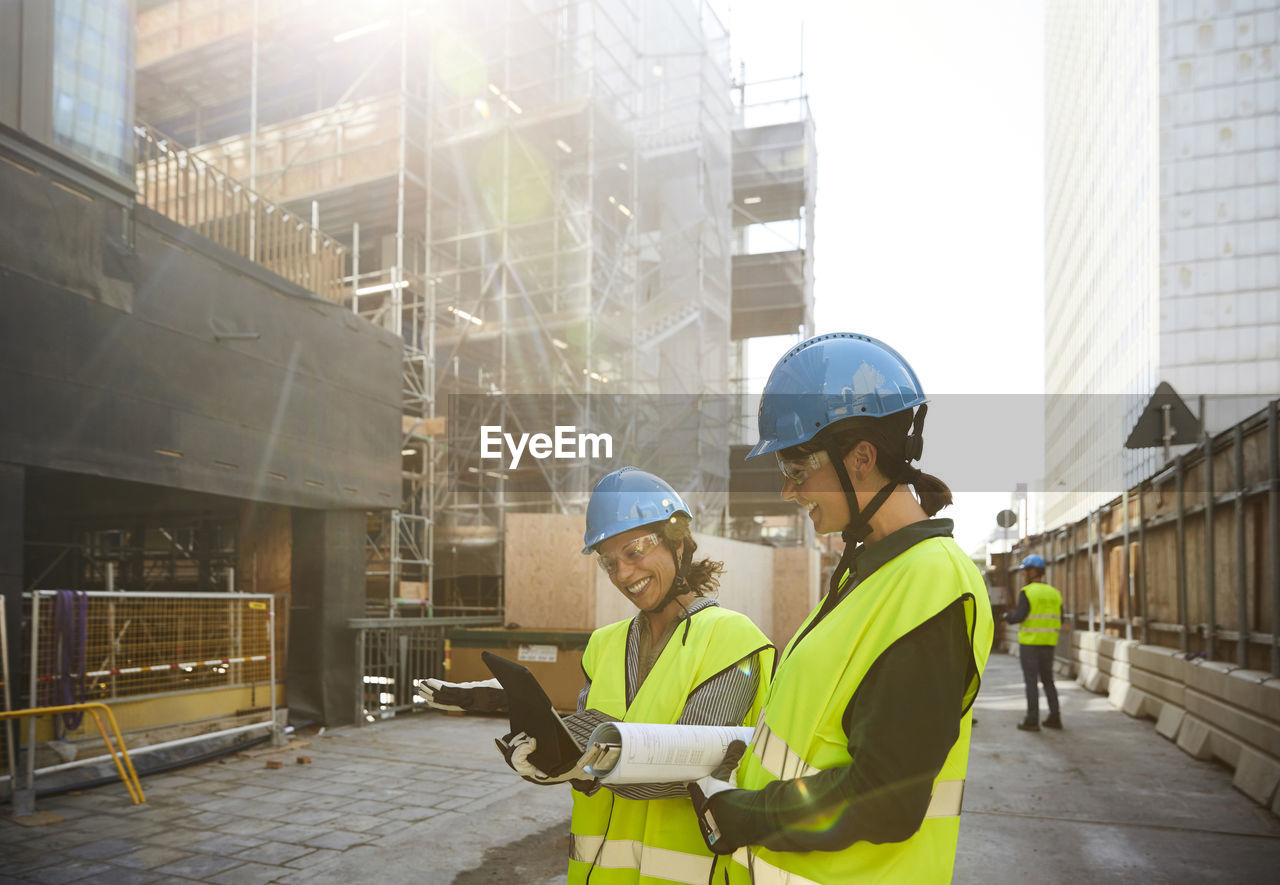 Female engineers discussing over digital tablet at construction site during sunny day