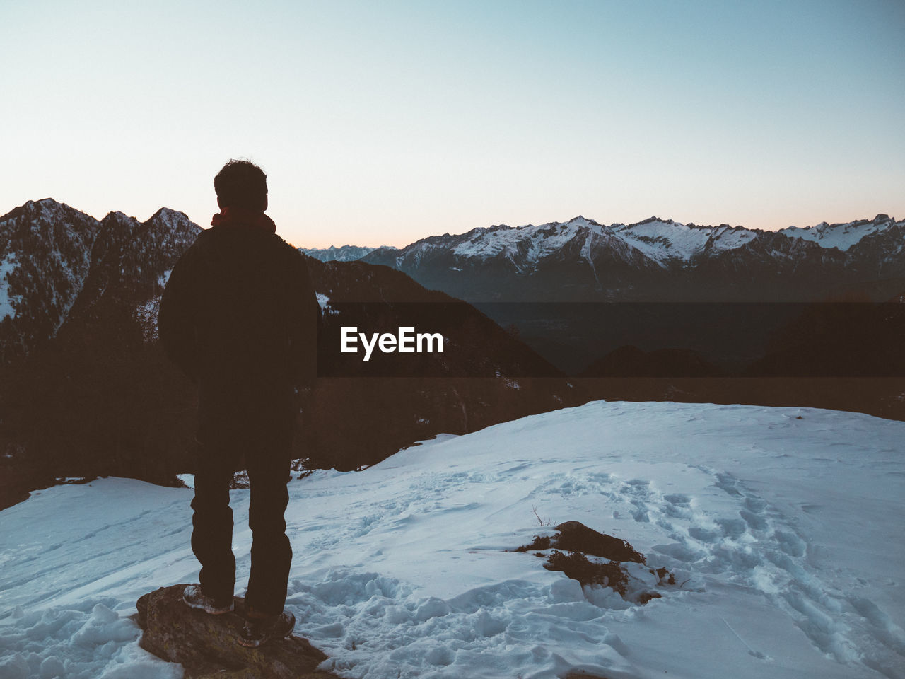 Rear view of man standing on snowcapped mountain against sky