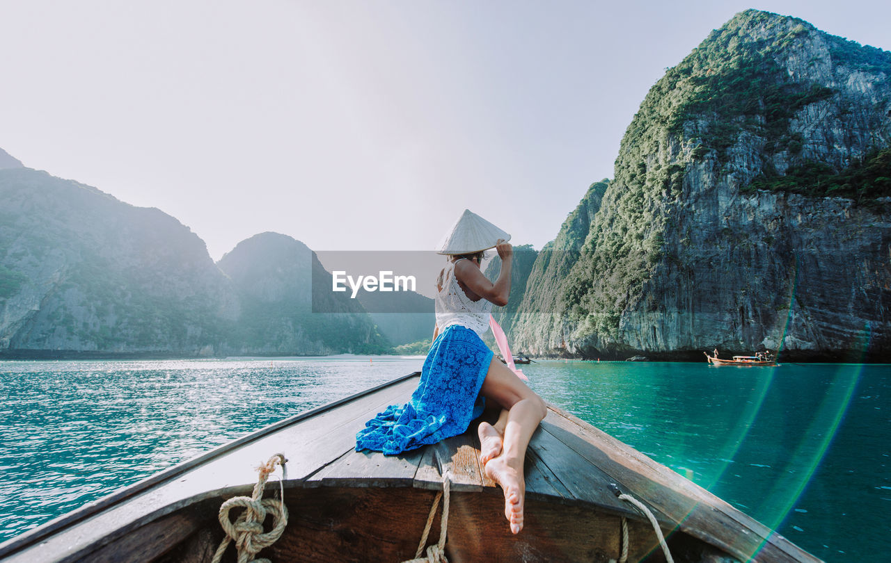 WOMAN SITTING ON SHORE AGAINST SKY