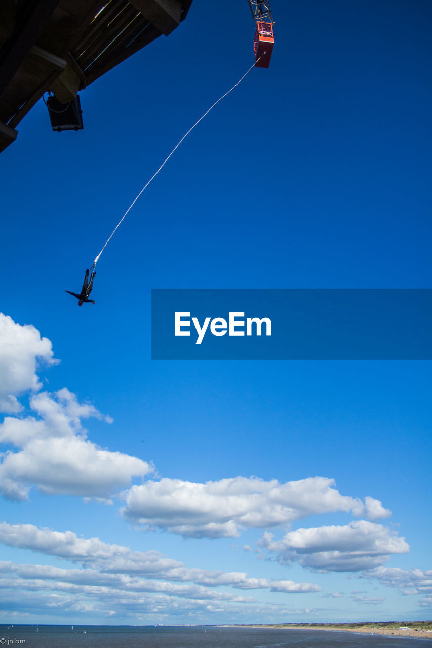 Person performing bungee jump against blue sky