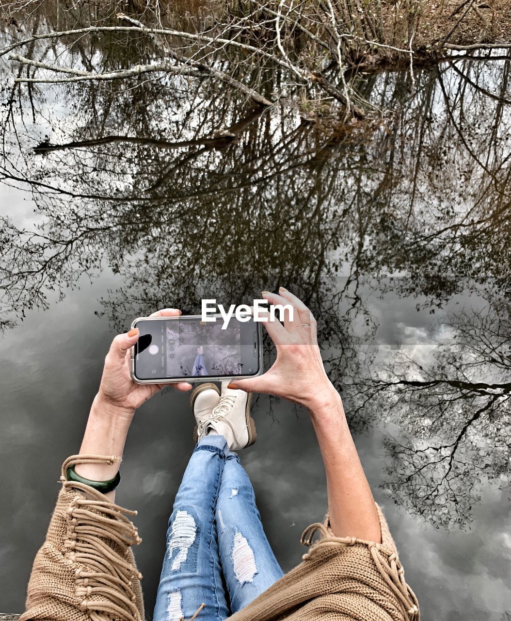 LOW SECTION OF PERSON PHOTOGRAPHING WITH MOBILE PHONE AGAINST TREES