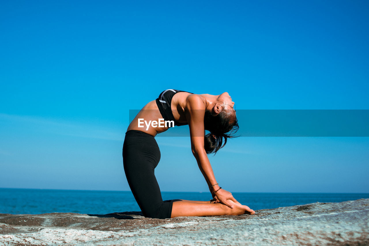 Woman practicing yoga at beach against sky