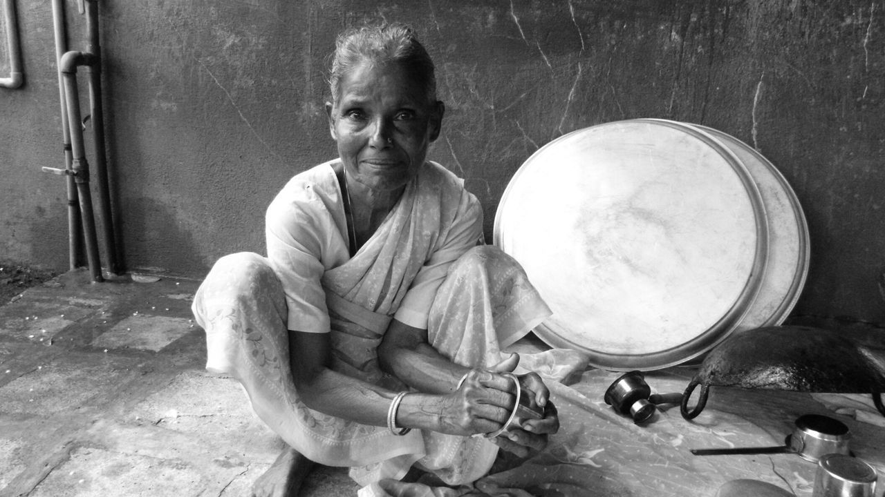 Portrait of senior woman washing utensils while crouching against wall