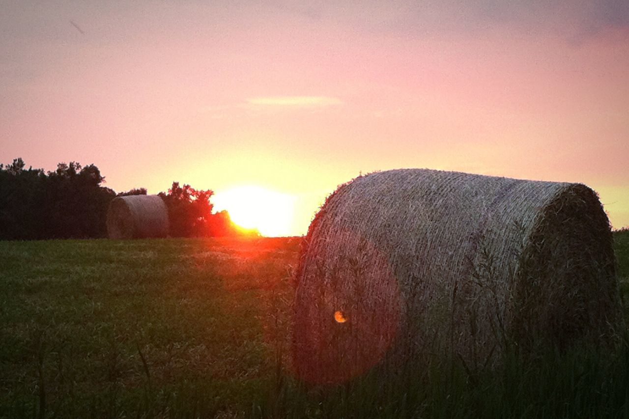 Hay bales on field against sky during sunset