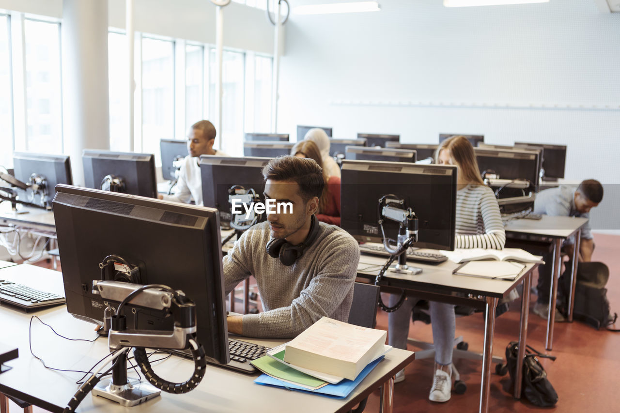 Male and female students using computers at library in university