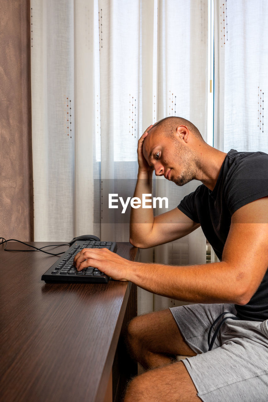 MIDSECTION OF MAN SITTING ON TABLE AT HOME