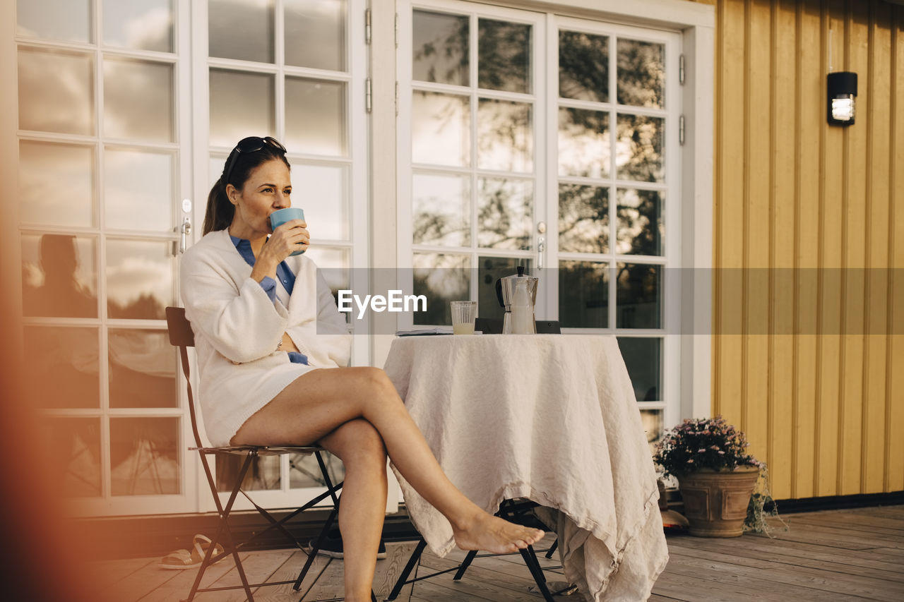 Full length of mature woman drinking coffee while sitting at patio in holiday villa