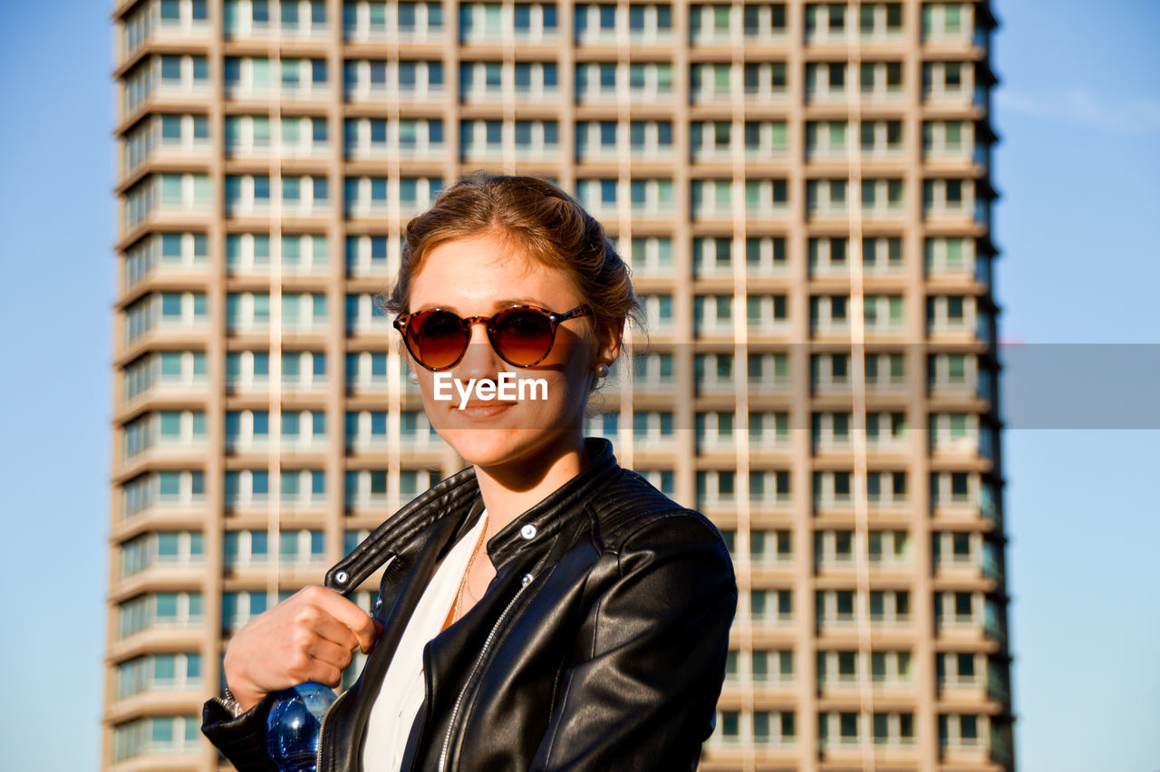 Portrait of young woman in sunglasses standing by building in city
