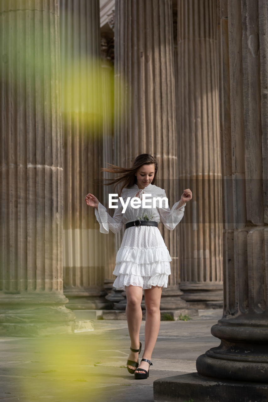 Full length of young woman standing against columns