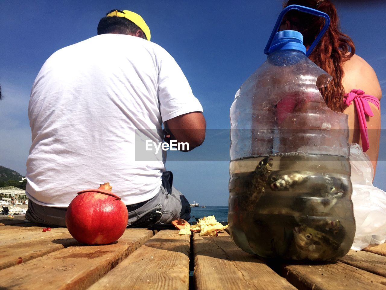 Rear view of man and woman sitting on pier with fishes in plastic jar