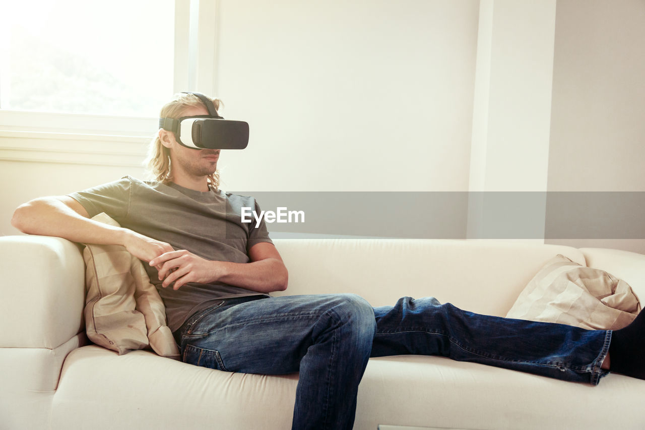 MIDSECTION OF MAN USING MOBILE PHONE WHILE SITTING ON SOFA