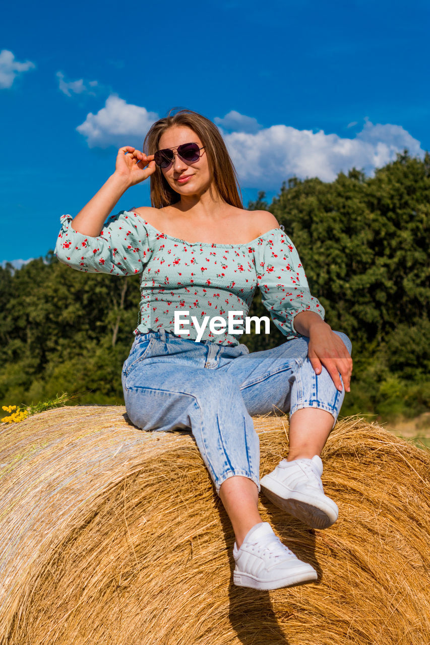 Young woman sitting on field against sky