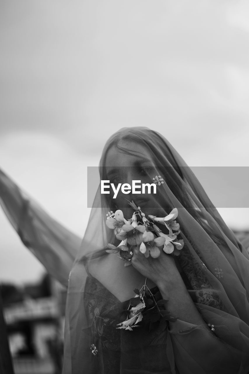 Midsection of woman holding flower standing against sky