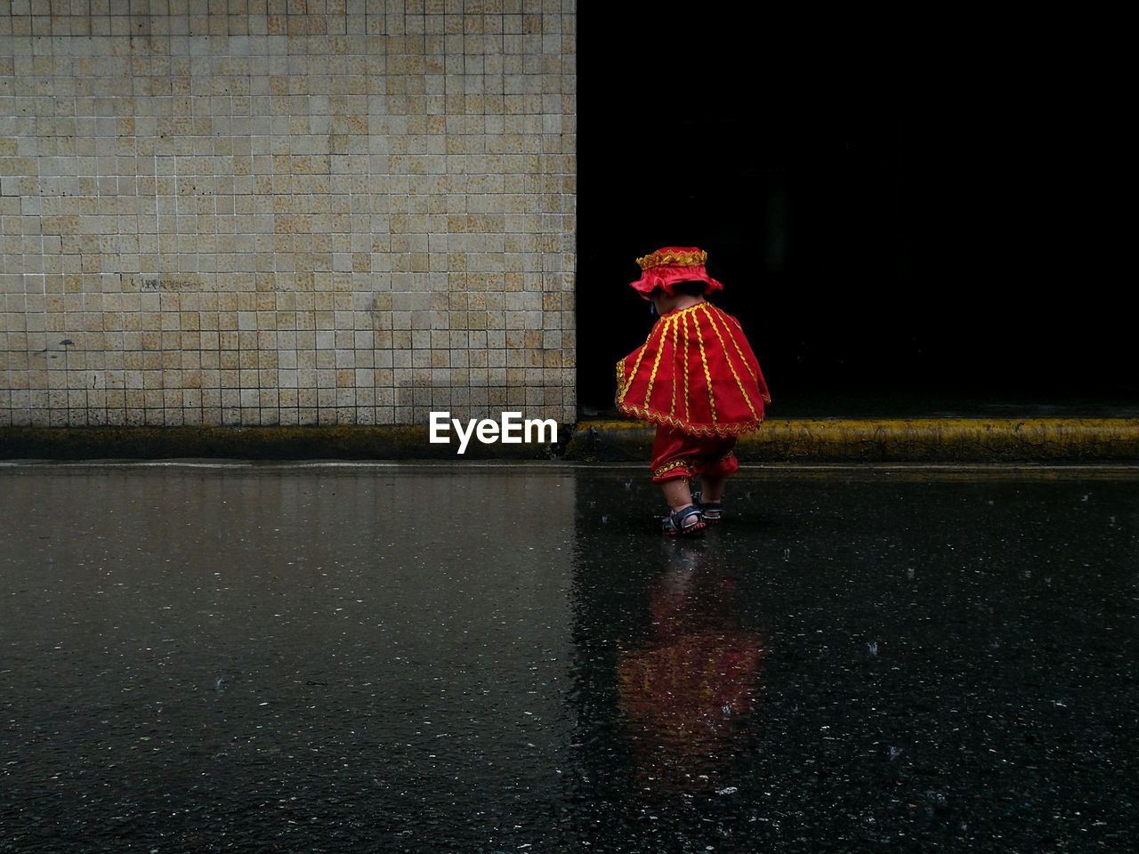 Rear view full length of child walking on road during rainy season