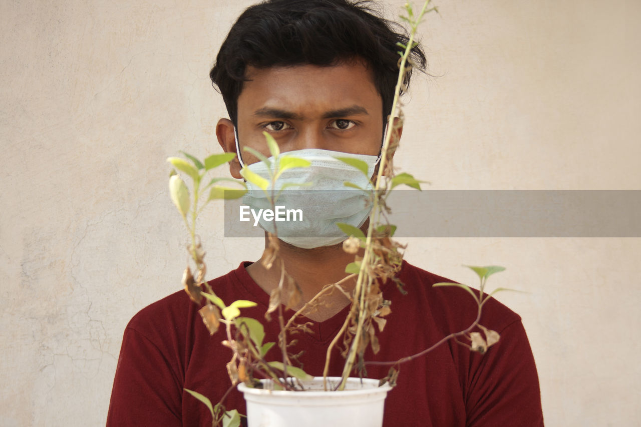 Portrait of young man holding plant against wall