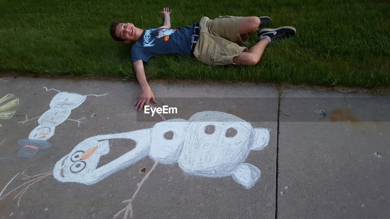 High angle view of young man lying on grassy field by drawing over road