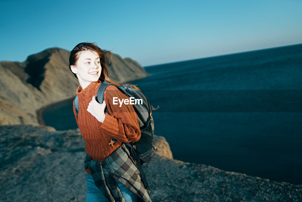 WOMAN STANDING ON ROCK AGAINST SEA